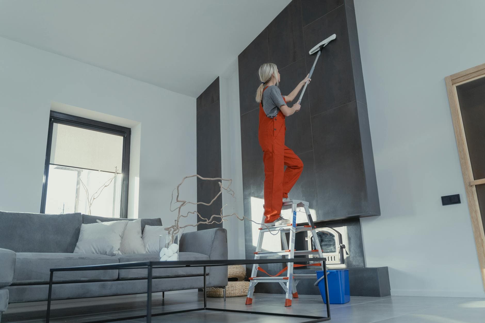 Long Island Maid cleaner in red overalls on a ladder cleaning a high wall in a Long Island apartment — Post-Construction Cleanup in Hempstead, Nassau County